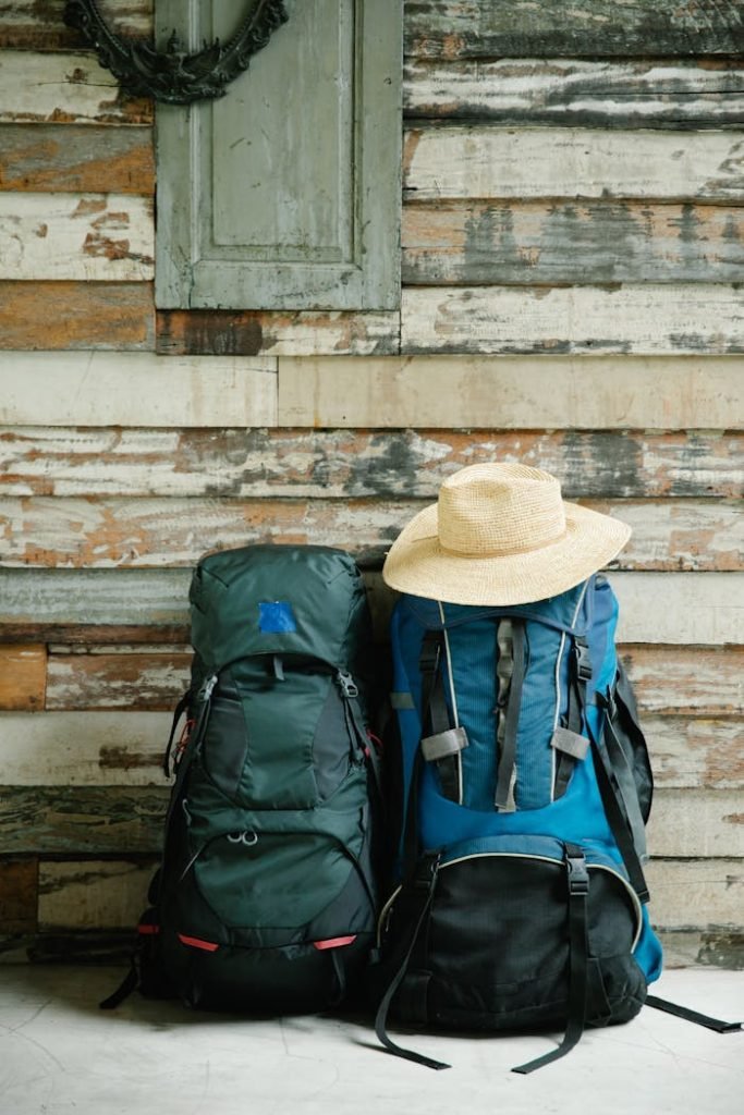 Two backpacks with a straw hat leaning against a rustic wooden wall.