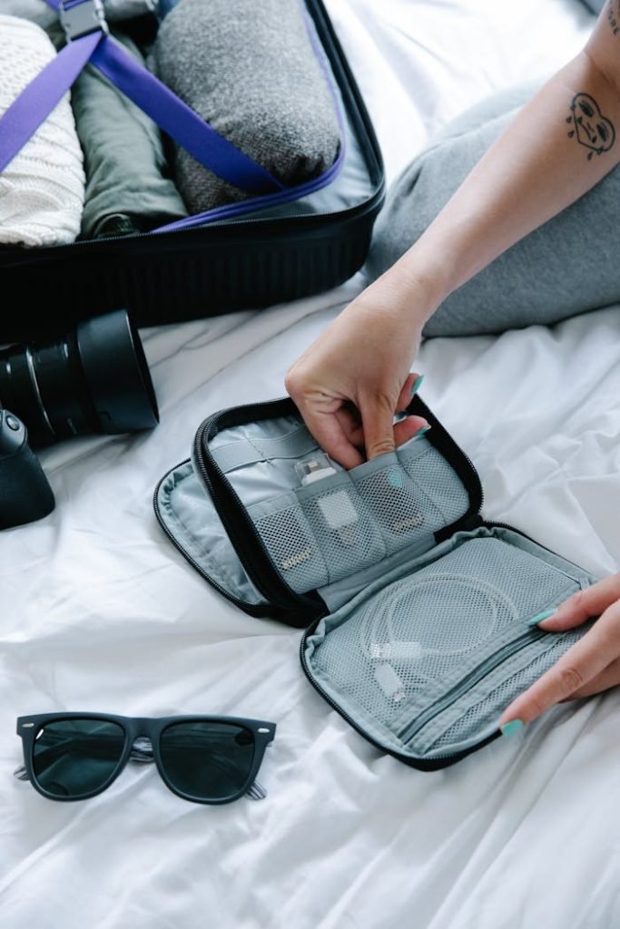 Close-up view of travel essentials including sunglasses and electronics organizer on a bed.