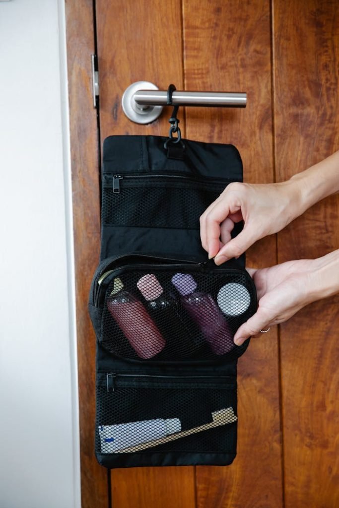 Travel toiletry bag organized with cosmetics, hanging on a wooden door handle.